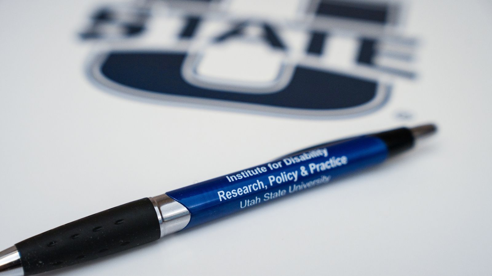 A branded Institute for Disability Research, Policy & Pen sits on top of a folder with a Utah State University logo.