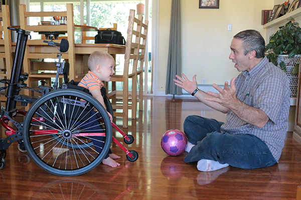 Toddler in wheelchair playing with man