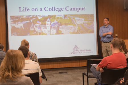 Sheen stands by a projection screen that reads, "Life on a College Campus"