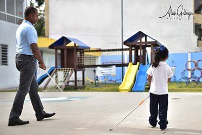 Pavithran and a young girl walk on a playground in Mexico using white canes
