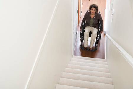 A woman in a wheelchair pauses at the bottom of a stairway