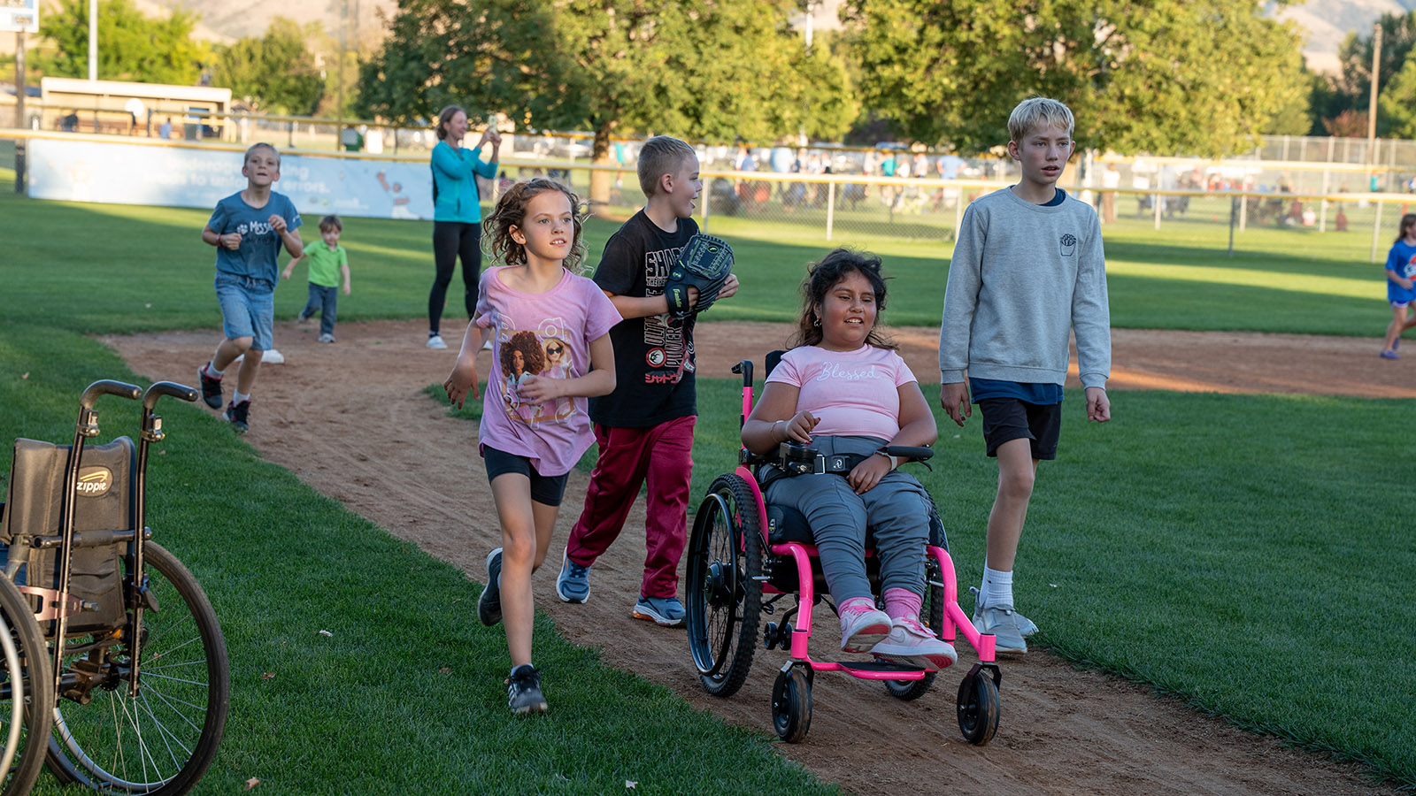 children, one of them in a wheelchair, move together over a baseball diamond