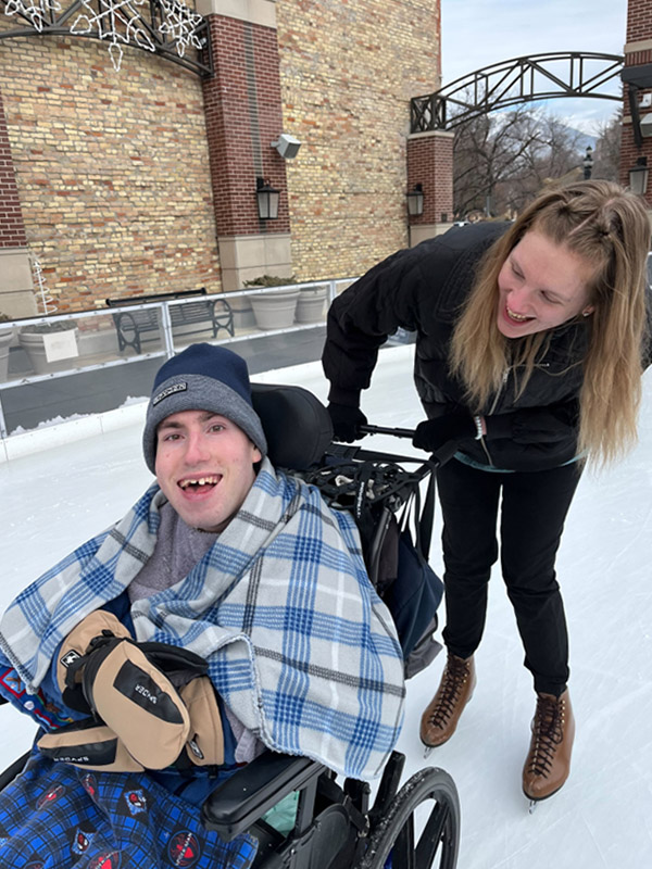 a woman in ice skates pushes a young man in a wheelchair