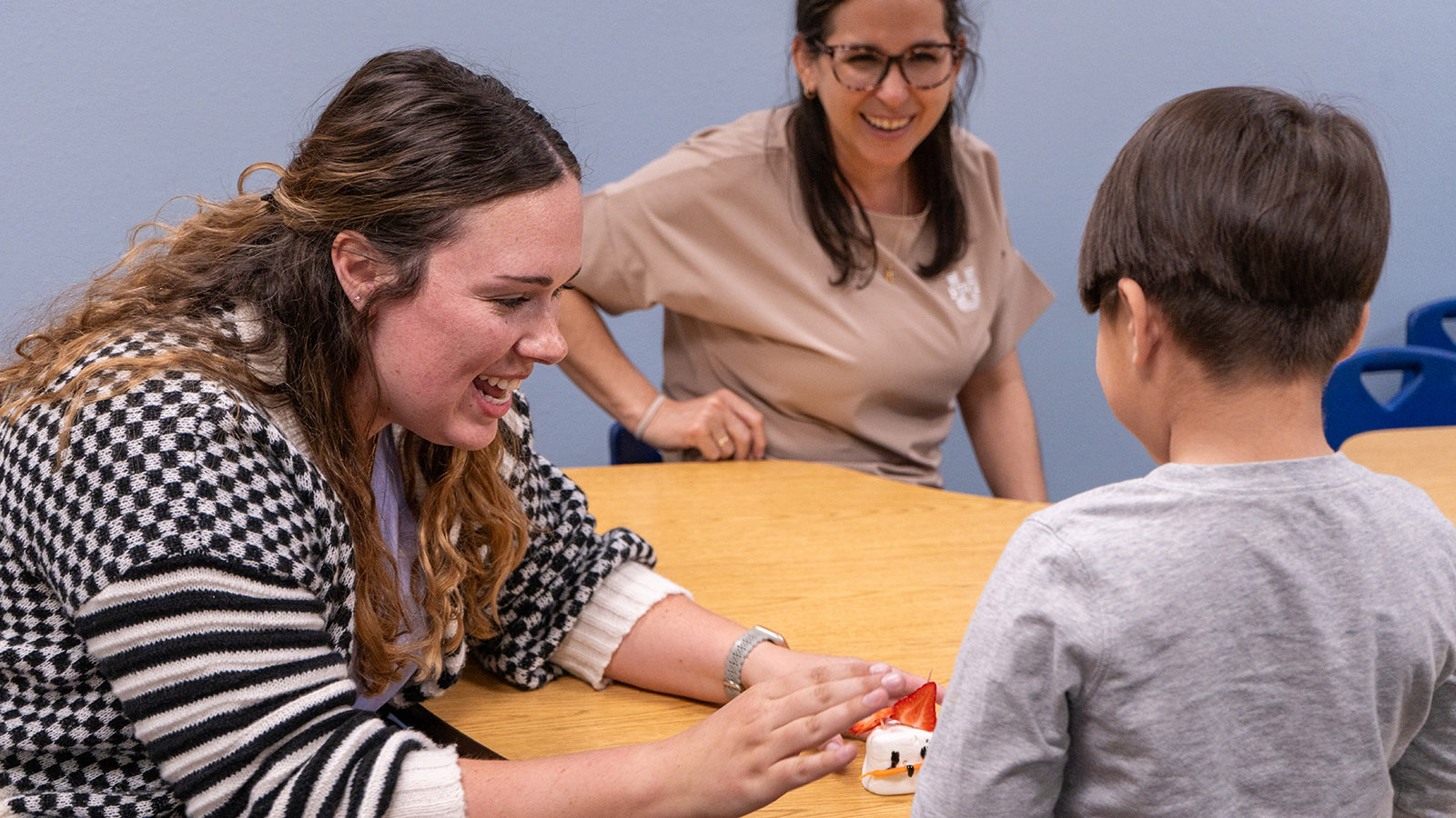 An NUHV staff person smiles at a child while another staff person celebrates in the background