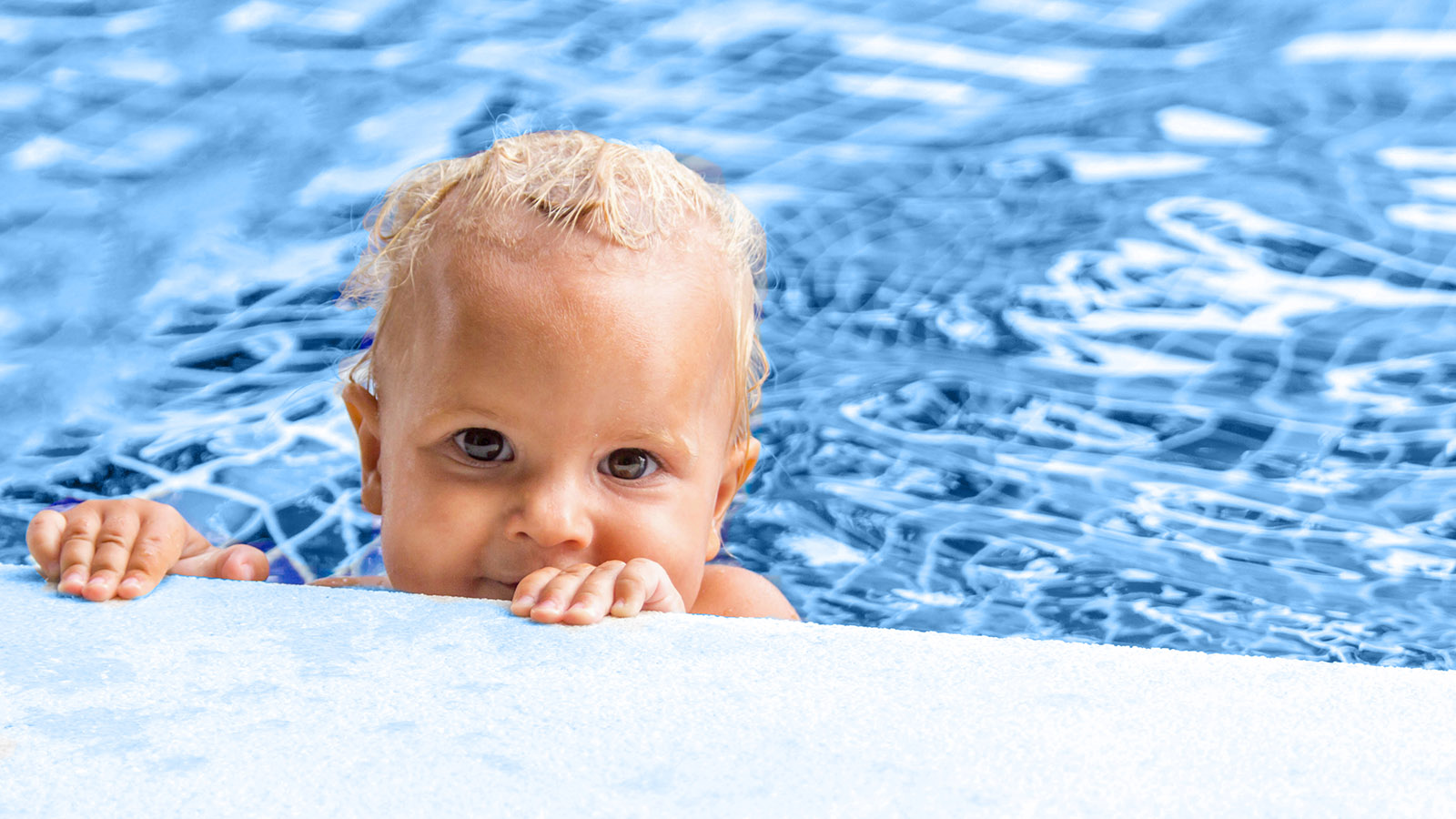 a toddler hangs onto the edge of a swimming pool