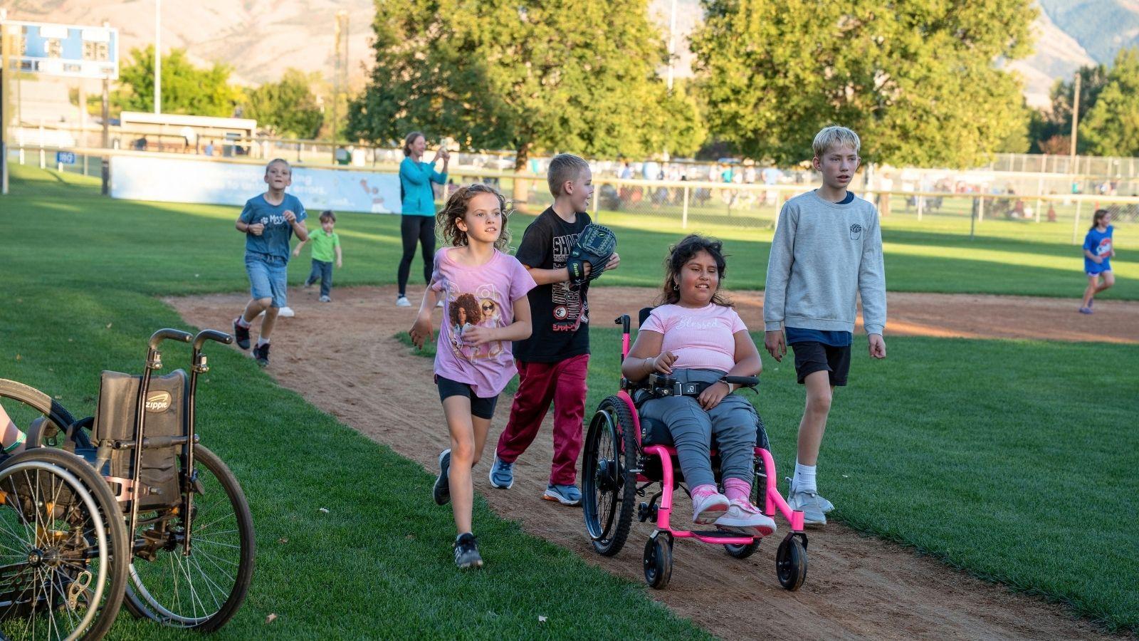 A group of people running to home plate on a baseball field. Some of them are using assistive technology such as a powered wheelchair.