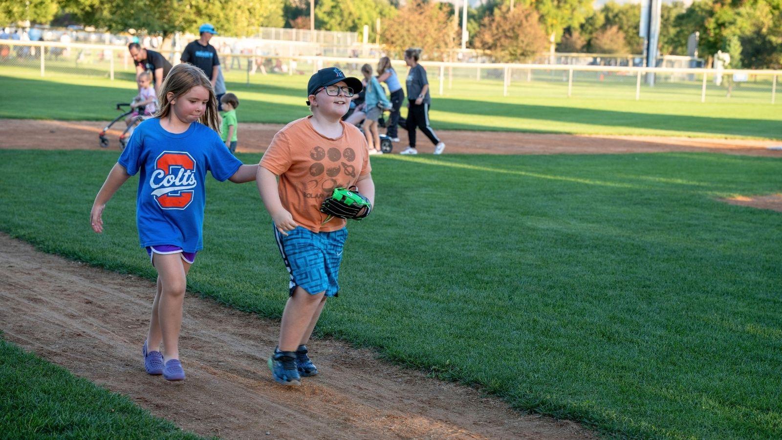 Two young individuals run to home plate on a baseball field.
