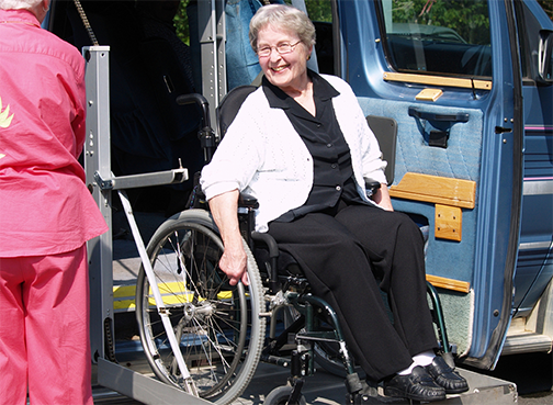 An elder woman on a wheelchair smiling while getting out of a equipped van